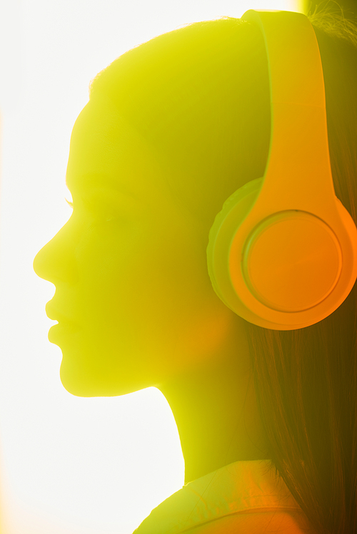 Side view of young woman listening to music in wireless headphones in bright light