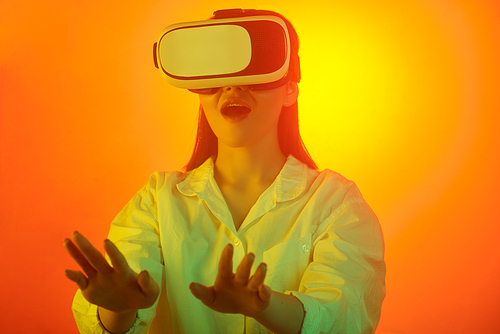 Excited young woman in blouse reaching hands while playing video game using virtual reality device