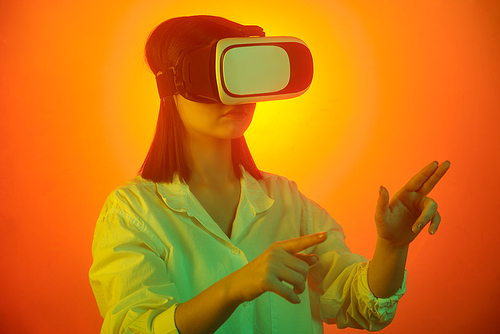 Young female student in vr headset pointing at virtual display while preparing presentation over neon background