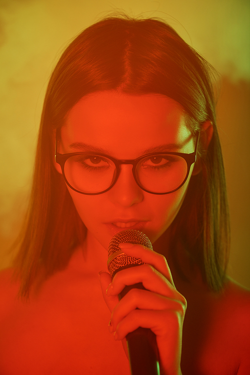 Sexy girl in eyeglasses singing song in microphone while having fun in smoky karaoke club