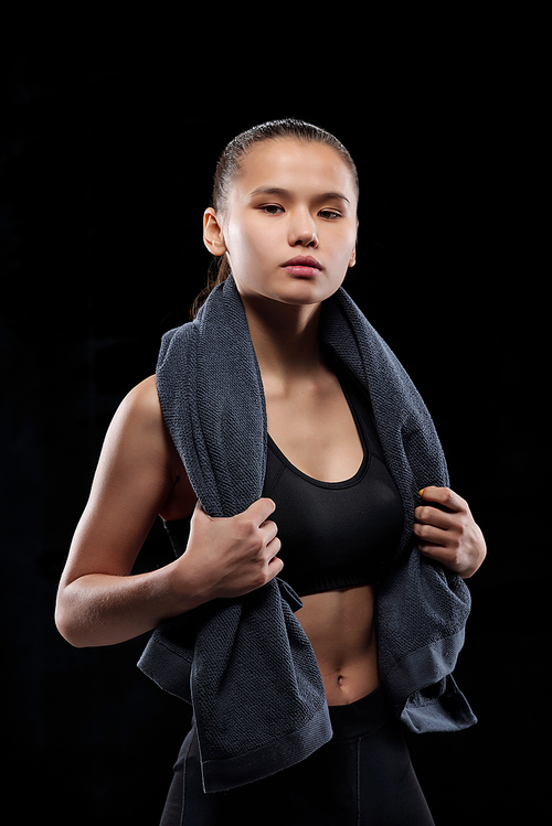 Pretty young female in black sportswear holding grey soft towel on her neck while looking at you in leisure center