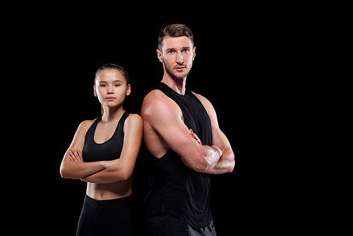 Young fit sportsman and sportswoman in black activewear standing close to one another with arms crossed by chest