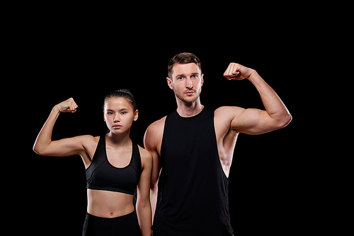 Young muscular sportsman and pretty fit female in activewear showing their strength while standing in front of camera