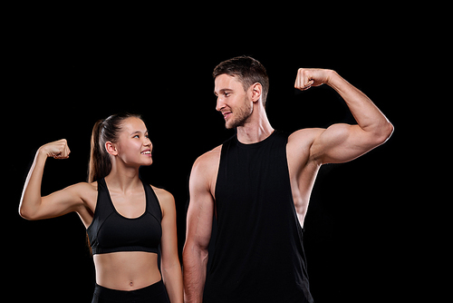 Young cheerful sports couple in activewear looking at each other while showing their strength in front of camera