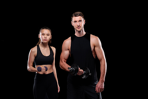 Young fit woman with dumbbell and muscular sportsman with barbell exercising in front of camera together