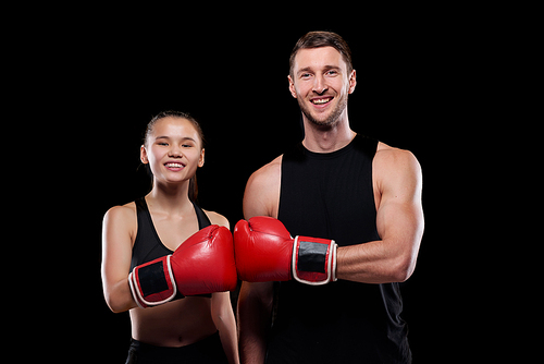 Happy young man and woman in activewear looking at you with smiles while touching each other hands in boxing gloves