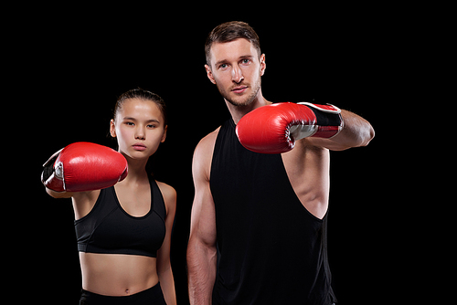 Young sportsman and sportswoman in activewear and boxing gloves training in front of camera against black background