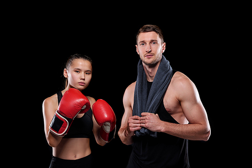 Sporty girl in red boxing gloves and her muscular boyfriend with towel standing close to each other in front of camera