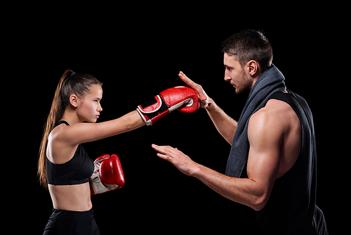 Young sportswoman in activewear and boxing gloves exercising with trainer consulting her about rules of fight