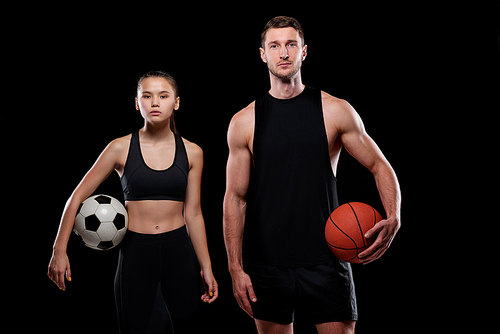 Young female soccer player and male basketballer in sportswear holding balls while standing in front of camera