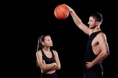 Young muscular basketball trainer holding ball over fit sportswoman looking at it and listening to the guy
