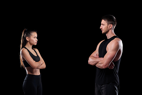 Young fit sportsman and sportswoman with crossed arms standing opposite each other on black background