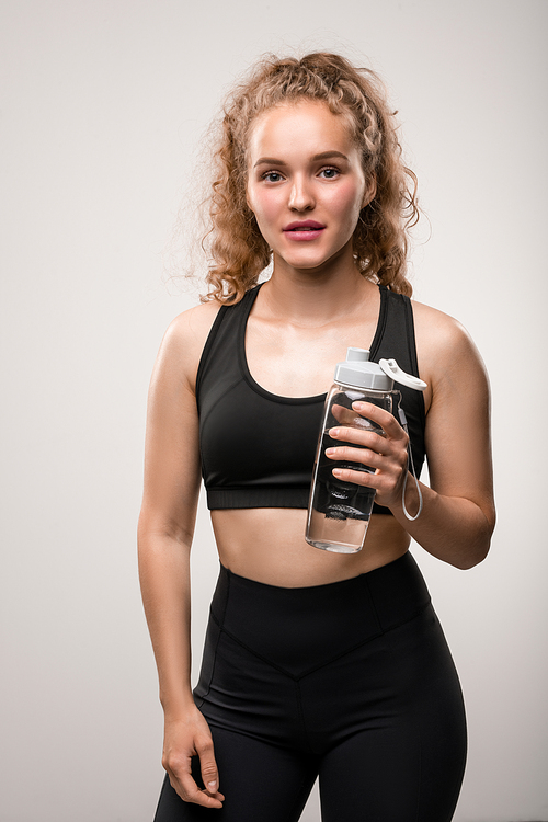 Young cheerful fit woman in black tracksuit holding plastic bottle of pure water while having break for refreshment after sports training