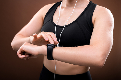Mid section of young sportswoman in activewear and earphones switching on her fitbit on wrist before outdoor jogging workout