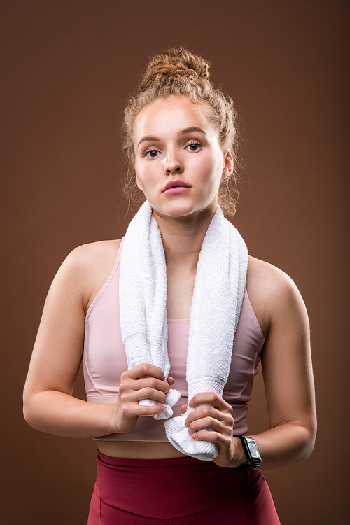 Fit young sportswoman with white soft towel on her neck having rest after physical training while standing in front of camera in isolation