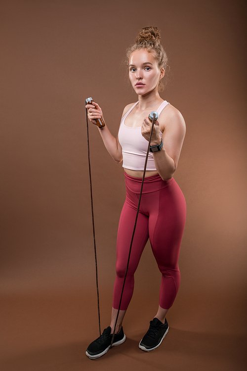 Pretty young fit sportswoman in activewear keeping right foot on skipping-rope while exercising in isolation in front of camera
