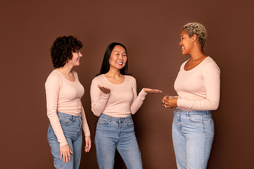 Group of three young smiling women in white pullovers and blue jeans chatting about their plans or curious stuff that happened recently