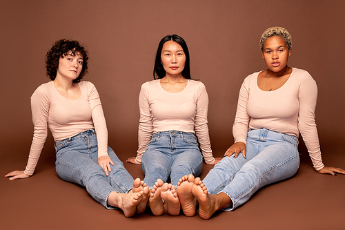Group of contemporary young casual females of various ethnicities sitting on the floor with their bare feet close to each others
