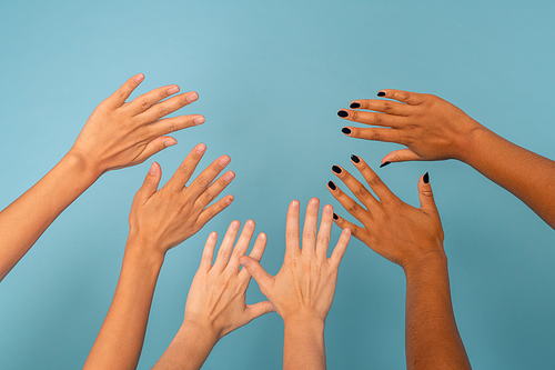 Three pairs of hands of young females of various ethnicities with different color of skin against blue background in front of camera