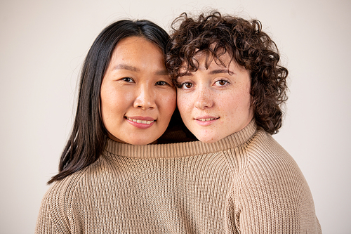 Young Asian and Caucasian women with dark hair in one knitted cotton sweater standing in front of camera against white background
