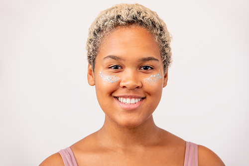 Happy young African female with undereye mask and toothy smile standing in front of camera against white background in isolation