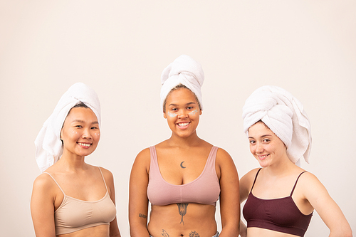 Cute Asian, African and Caucasian girls with soft towels on heads and tanktops standing in front of camera over white background