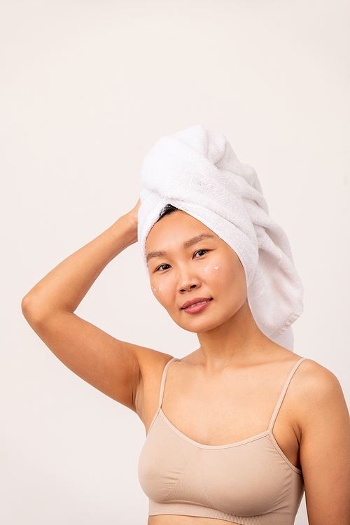 Young pretty female of Asian ethnicity with towel on head and beige tanktop relaxing in front of camera after morning shower