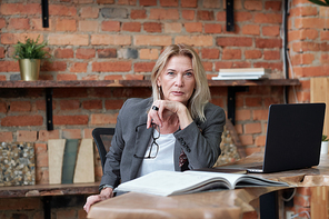 Portrait of serious mature female accountant with eyeglasses analyzing notes in ledger