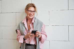 Portrait of happy successful mature businesswoman with sweater on shoulders using modern phone