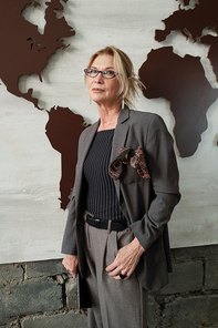 Portrait of serious confident businesswoman in stylish suit standing against world map banner