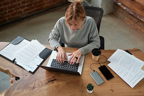 Above view of busy mature woman sitting at table with papers and devices and working hard in office