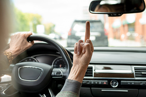 Hand of busy and annoyed mature businesswoman showing rude gesture to someone while holding by steer and driving home or to work