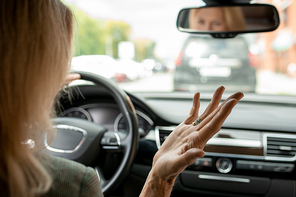 Hand of irritated and tired mature businesswoman with blond hair expressing annoyance with the car standing in front of hers