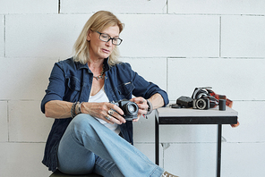 Modern mature lady photographer with blond hair checking camera before photo shoot in studio