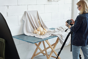Rear view of mature lady in denim jacket photographing vegetable against fabric in photo studio