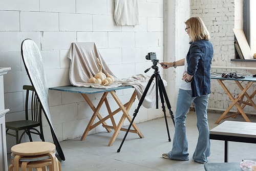 Rear view of mature lady in denim jacket photographing vegetable against fabric in photo studio