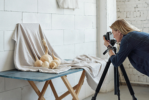 Busy mature photographer using camera on tripod while making creative photo of food in studio