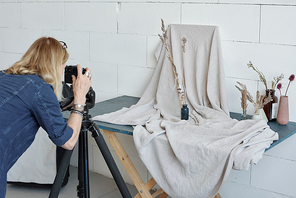 Rear view of busy creative woman using camera on tripod while photographing vase composition in studio