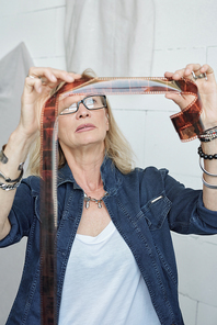 Portrait of confident mature photographer in denim jacket standing at table and choosing photos for album