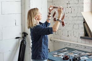 Mature lady with bracelets watching film tape against light while choosing footage
