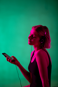 Excited blond girl in headphones and black leotard choosing and her favorite music in playlist in smartphone and enjoying it in isolation