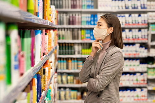 Hand of aged female consumer taking plastic bottle of fresh sour dairy drink while choosing food products in supermarket