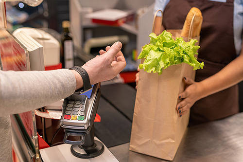 Hand of contemporary mature male consumer with smartwatch over screen of payment machine standing by cashier counter in supermarket