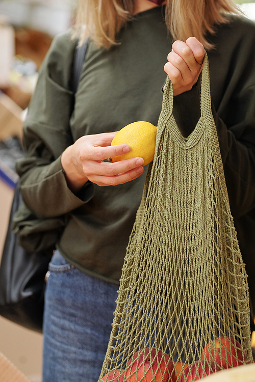 Close-up of unrecognizable woman putting lemon into net bag while buying it at food market