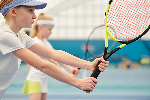 Serious and concentrated teenage girl in activewear standing on stadium and holding tennis racket ready to push the ball during play
