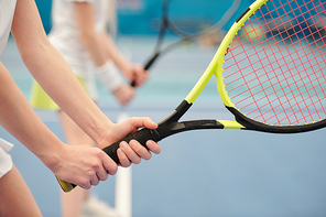 Hands of active Caucasian teenage girl standing on stadium against field and holding tennis racket ready to push the ball during play