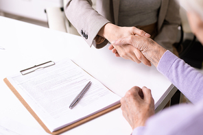 Close-up of unrecognizable social worker handshaking with elderly lady after signing document