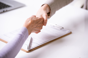 Close-up of advisor making handshake with retired woman after signing document