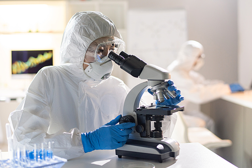 Female lab worker or researcher looking at new chemical element or virus molecule in microscope during scientific study