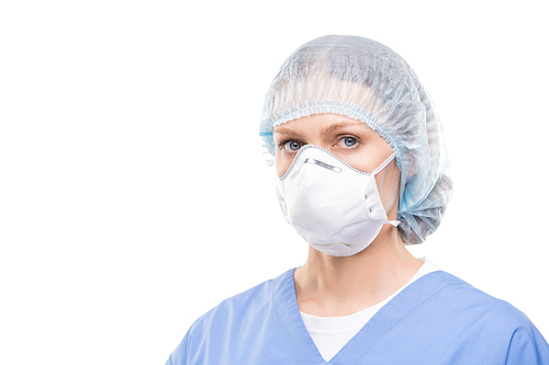 Contemporary young female doctor or nurse in protective mask and uniform standing in front of camera in isolation and looking at you